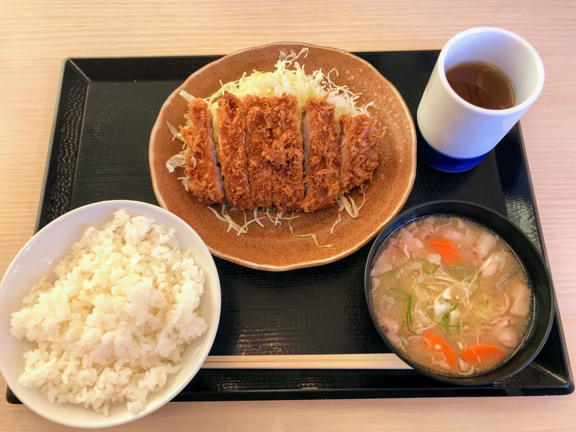 揚げたてのロースかつにキャベツの千切りが添えられ、ご飯と豚汁がセットになった、美味しそうなかつやのロースかつ定食の画像。