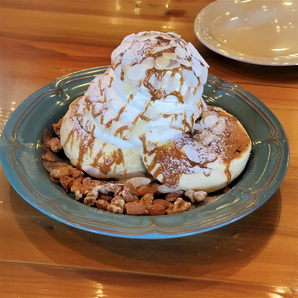 フワフワとしたパンケーキ(ホットケーキ)が皿に盛り付けられ、ホイップクリームとシロップが添えられている美味しそうな画像。